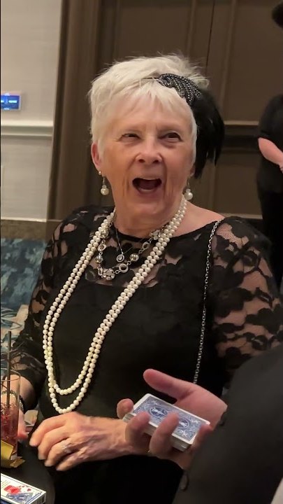 A guest at a gala reacting to close-up magic, a deck of cards in her hand