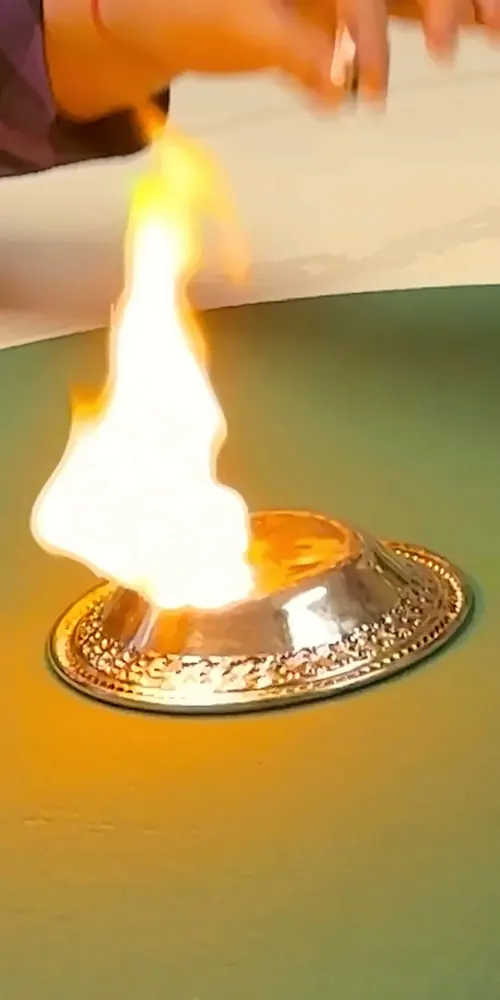 A ball of flame rising from a small silver dish on a green table, The Wizard's hand just above it
