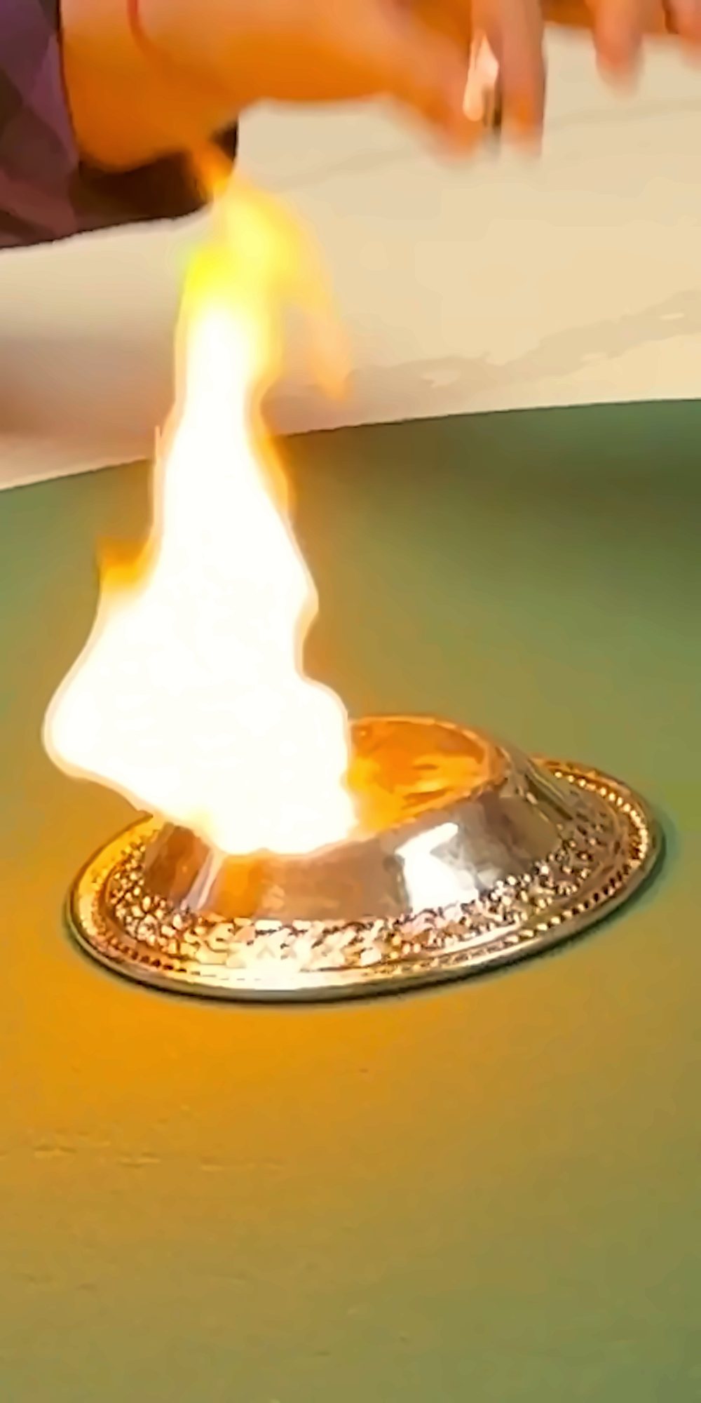 A ball of flame rising from a small silver dish on a green table, The Wizard's hand just above it