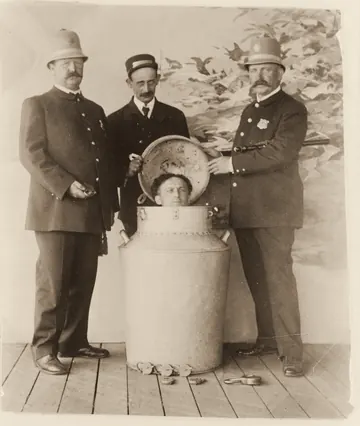 Three policemen stand around a giant milk can. Houdini's head pokes out of the top.